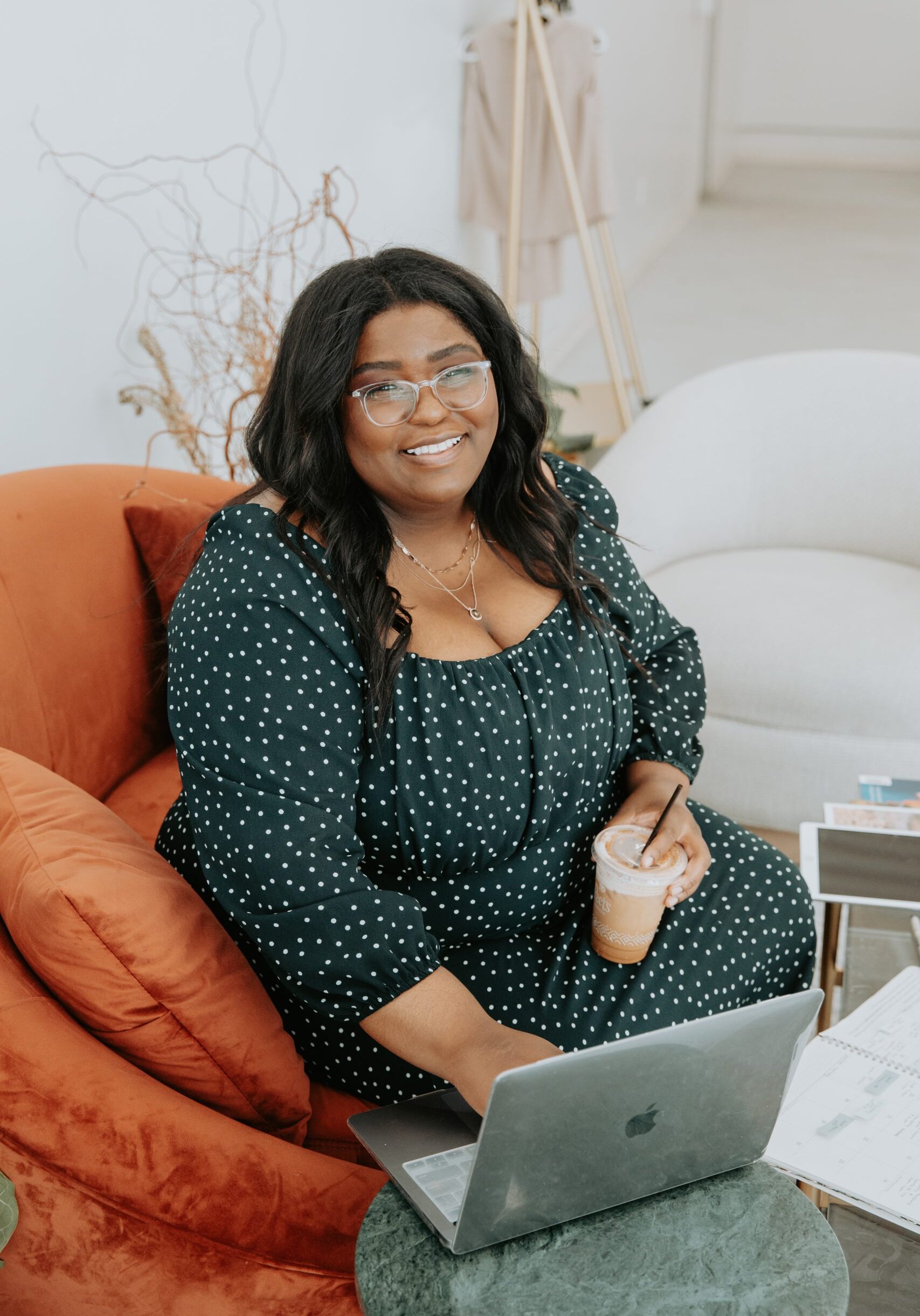 lady sitting on a couch with a laptop and holding a drink